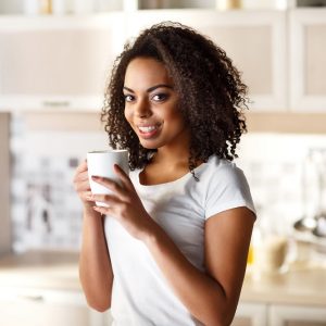 With positivity in mind.  Cheerful positive attractive girl holding cup and drinking tea while resting in the kitchen