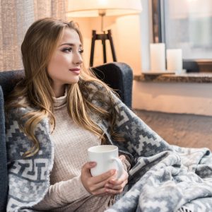thoughtful young woman in warm plaid with cup of hot drink