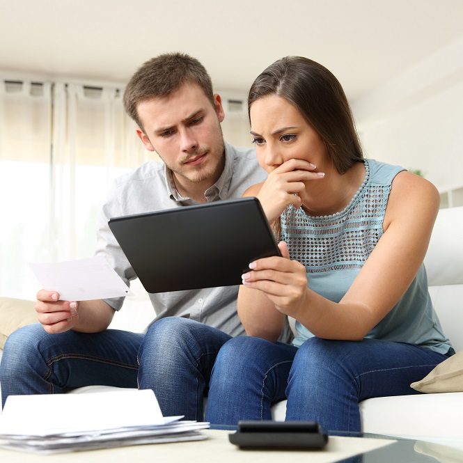 Worried couple checking bank account trouble online in a tablet sitting on a couch in the living room at home
